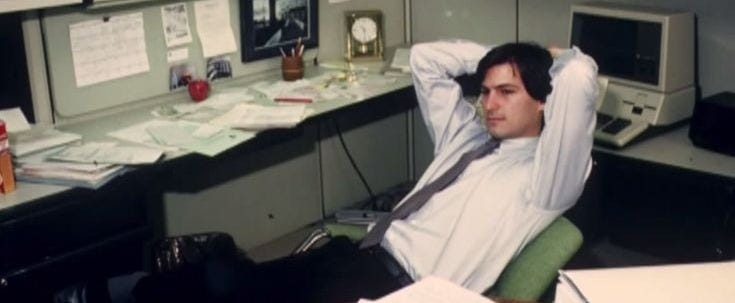 Steve Jobs leaning back at a desk, hands behind his head
